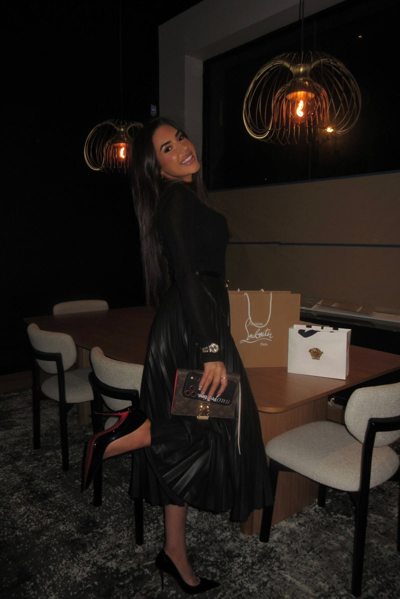 Woman in a black dress posing in a dimly lit room with modern decor.