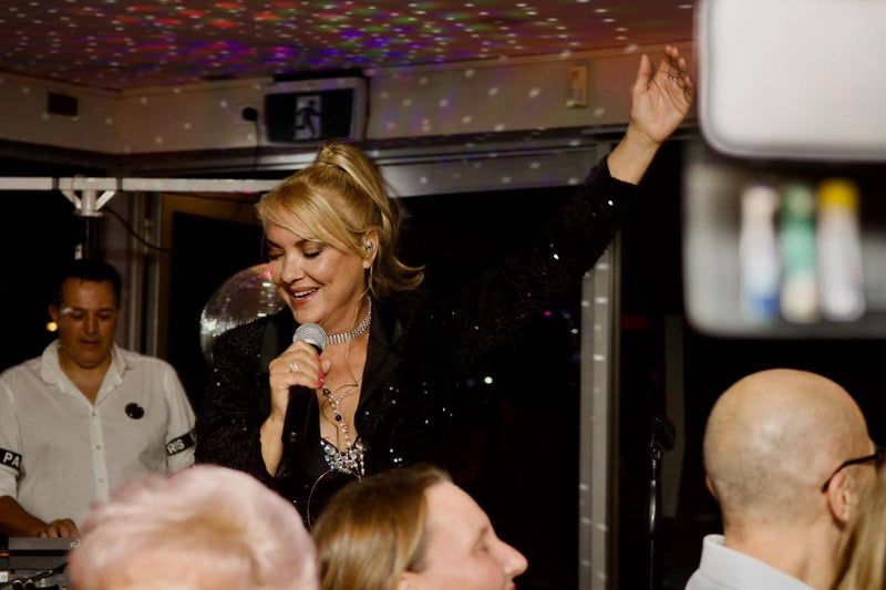 Woman singing into a microphone at a party with disco lights and people in the background