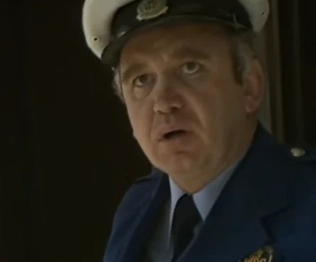 Officer wearing a navy uniform with a cap in a dimly lit setting