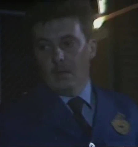 Officer wearing a uniform with a badge in a dimly lit setting