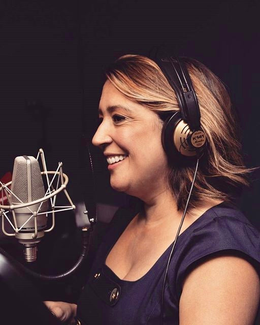 Woman wearing headphones and smiling in front of a microphone in a recording studio.