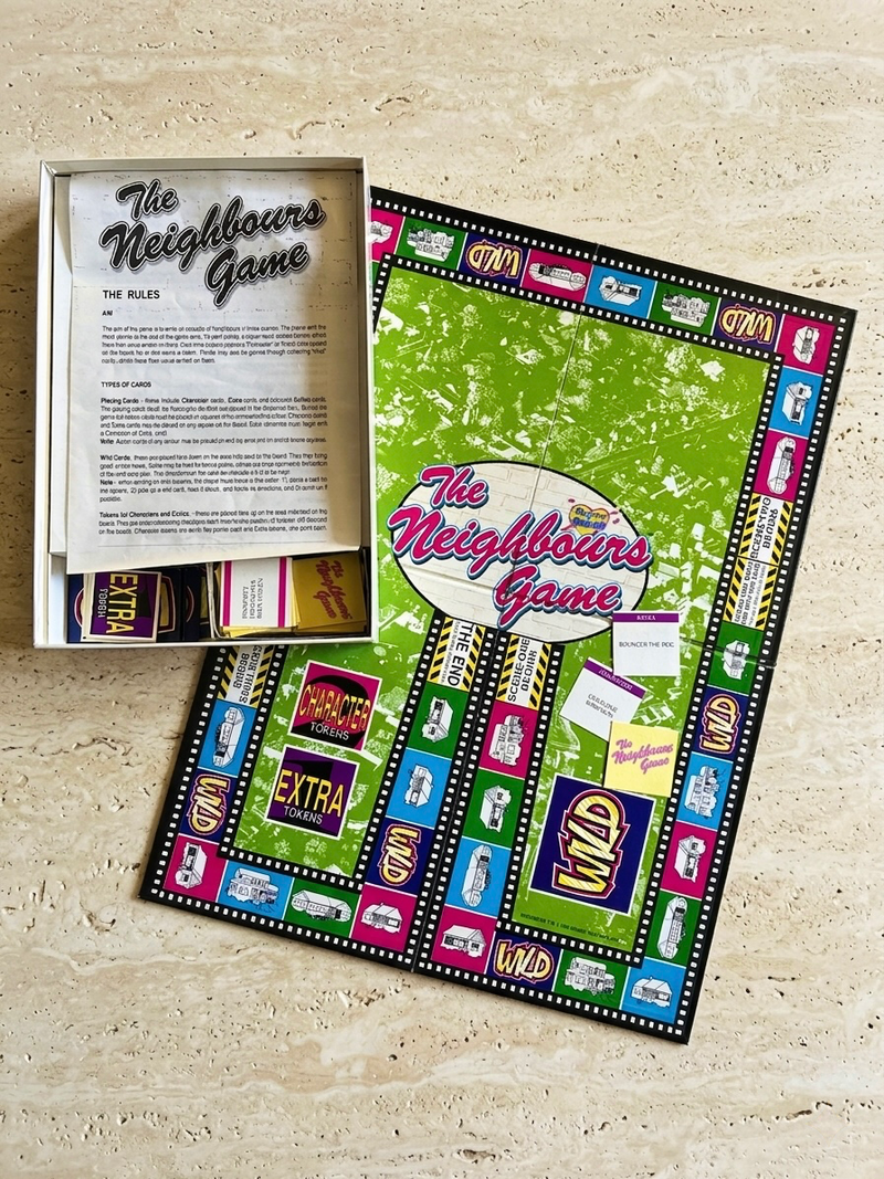 Board game packaging for 'The Neighbours Game' on a beige surface