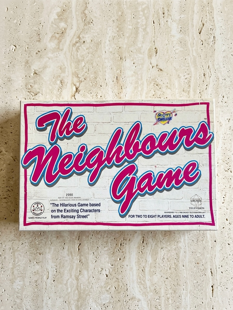 Board game box titled 'The Neighbours Game' on a textured surface