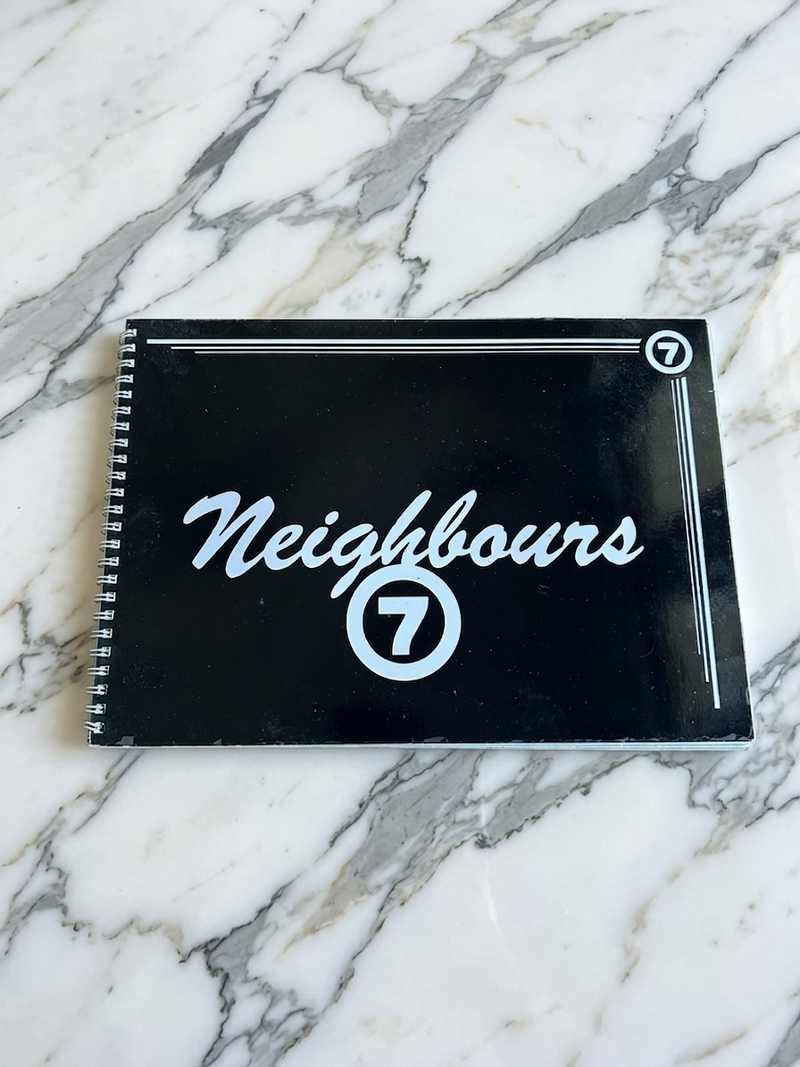 Black notebook with 'Neighbours 7' on a marble surface