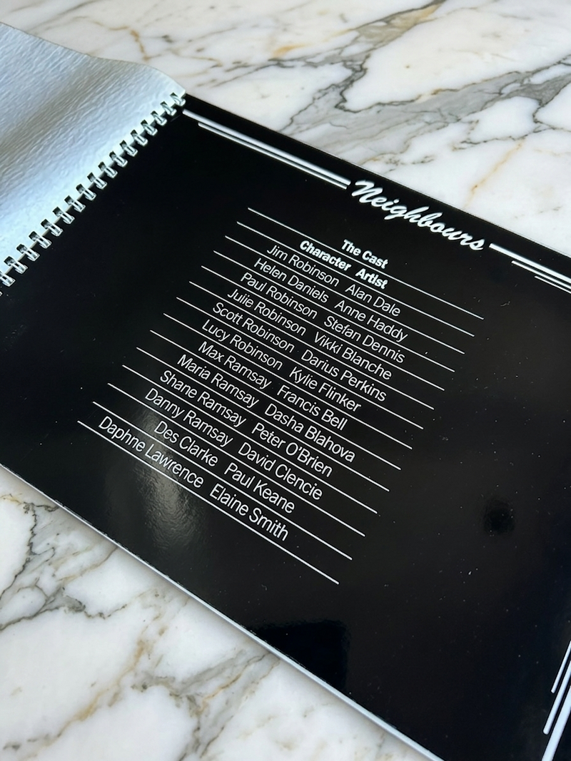 Black book with 'Neighbours' cast list on a marble surface