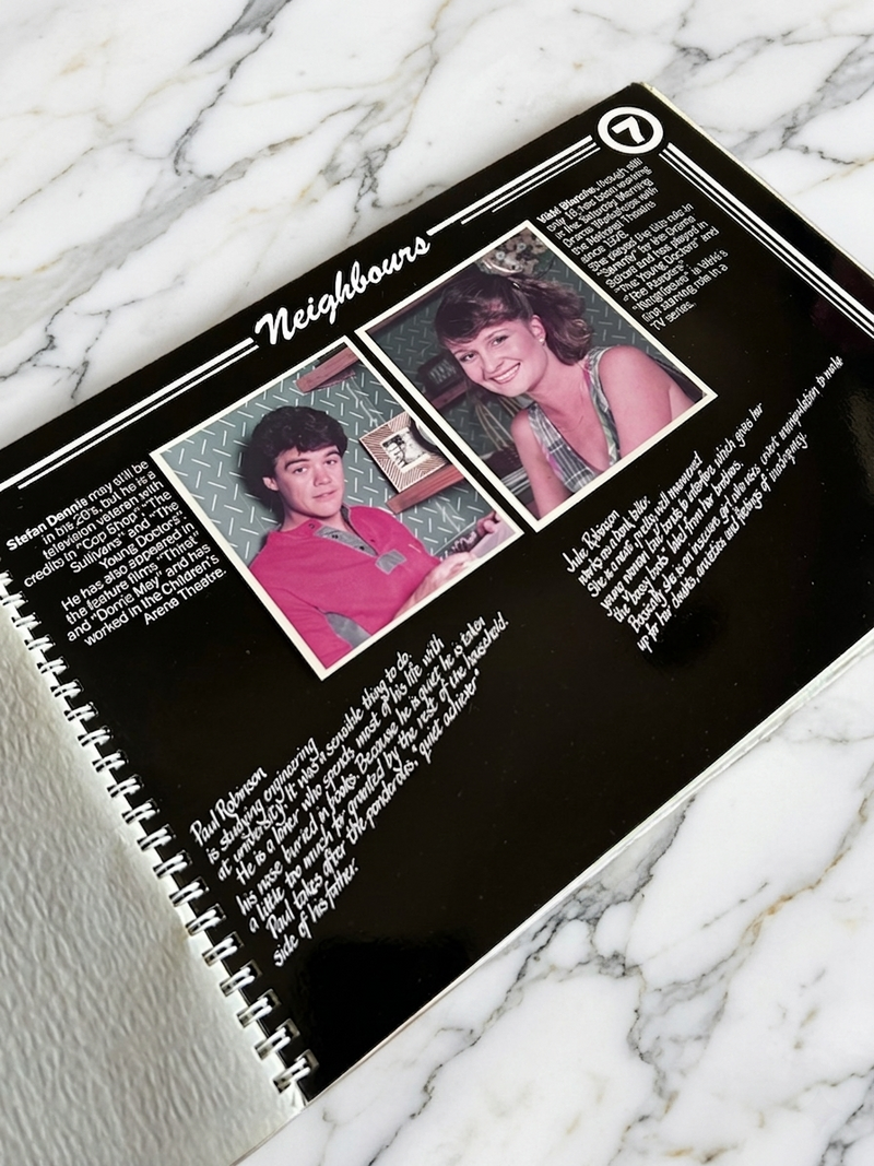 Spiral-bound book or notebook with 'Neighbours' cover featuring two people on a marble surface