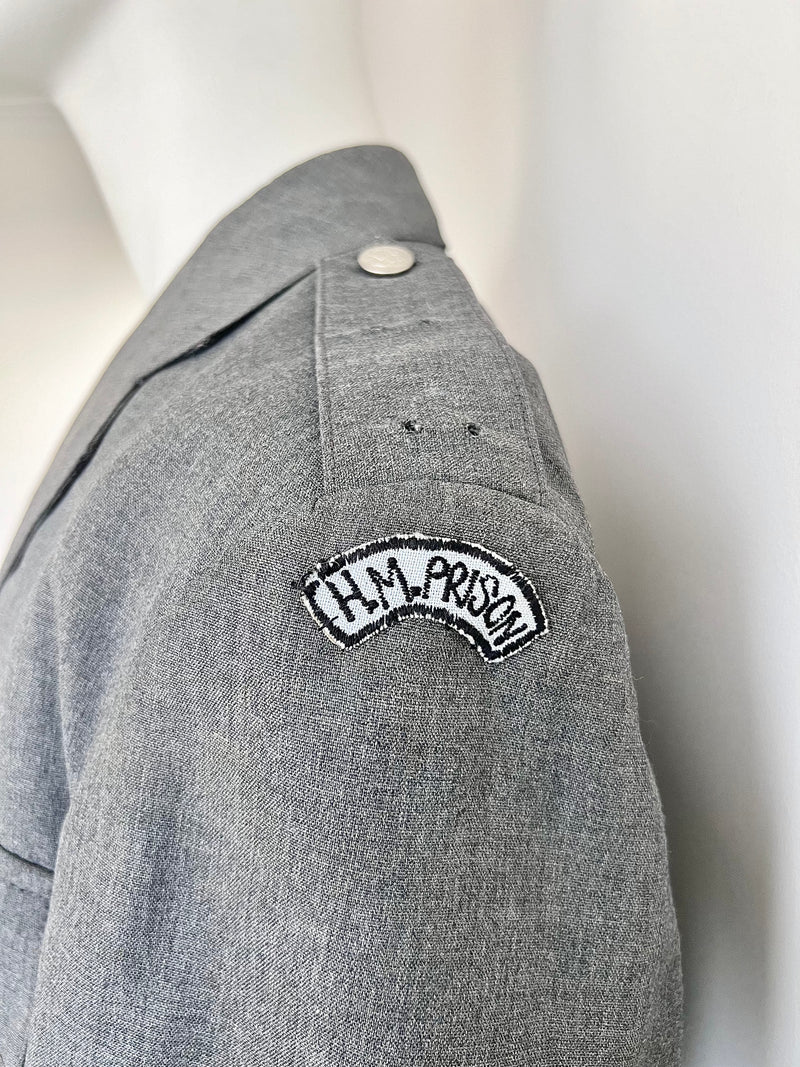 Gray jacket with 'H.M. Prison' patch on a mannequin against a white background