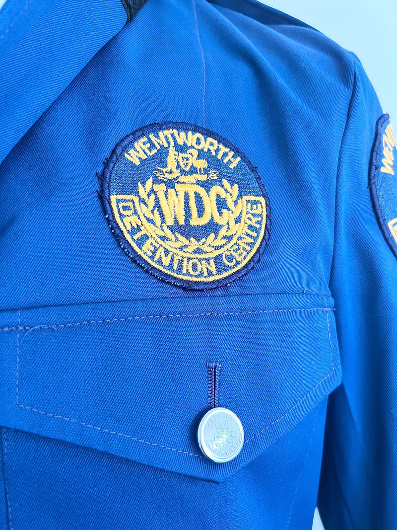 Blue guard jacket with a Wentworth Detention Centre patch on a light blue background