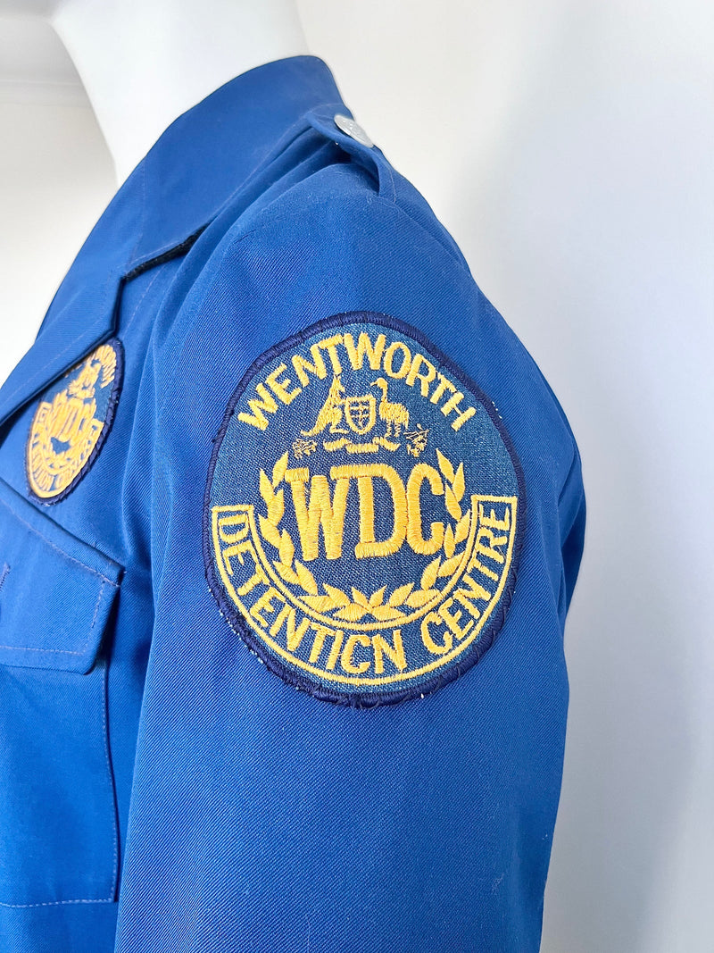 Blue guard jacket with Wentworth Detention Centre patch on a mannequin against a white background