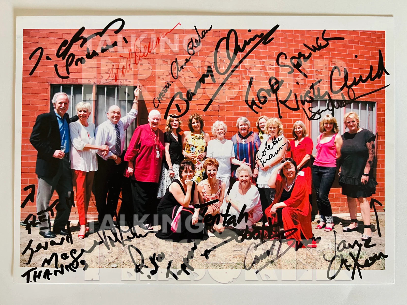 Group photo of people in front of a brick wall with autographs on the border.