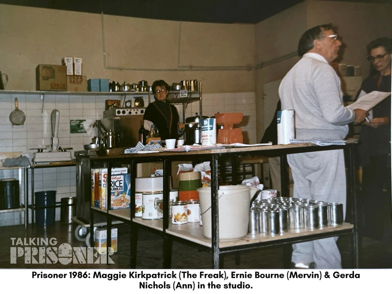 People in a kitchen setting with various items on shelves and counters.