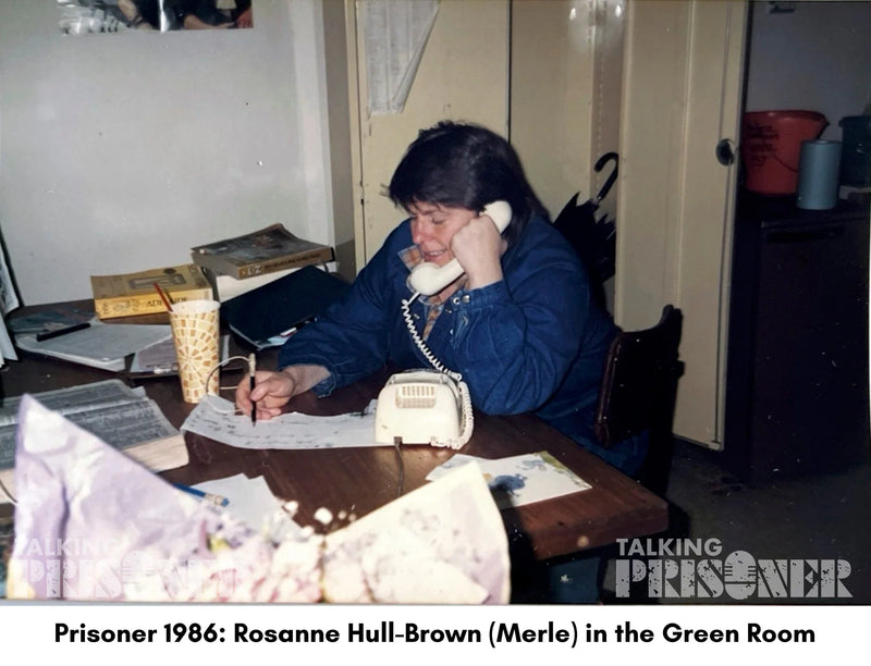 Person sitting at a desk with a phone, pen, and papers in a room labeled 'Green Room'.