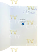 An open book or booklet showing an interior page with gold 'TV' logos repeated, a blue handwritten signature at the top right, and printed text reading 'FROM THE WORD GO!!' with a small blue circular logo in the center. The page is photographed against a white background.
