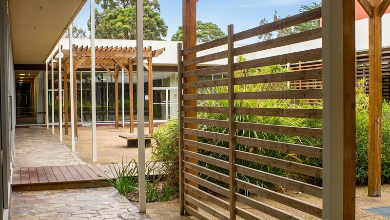 Outdoor patio area with wooden pergola and lattice fence, surrounded by greenery.