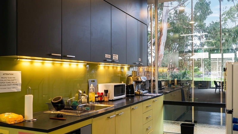 Modern kitchen with black countertops and light green cabinets, featuring a microwave and coffee maker.