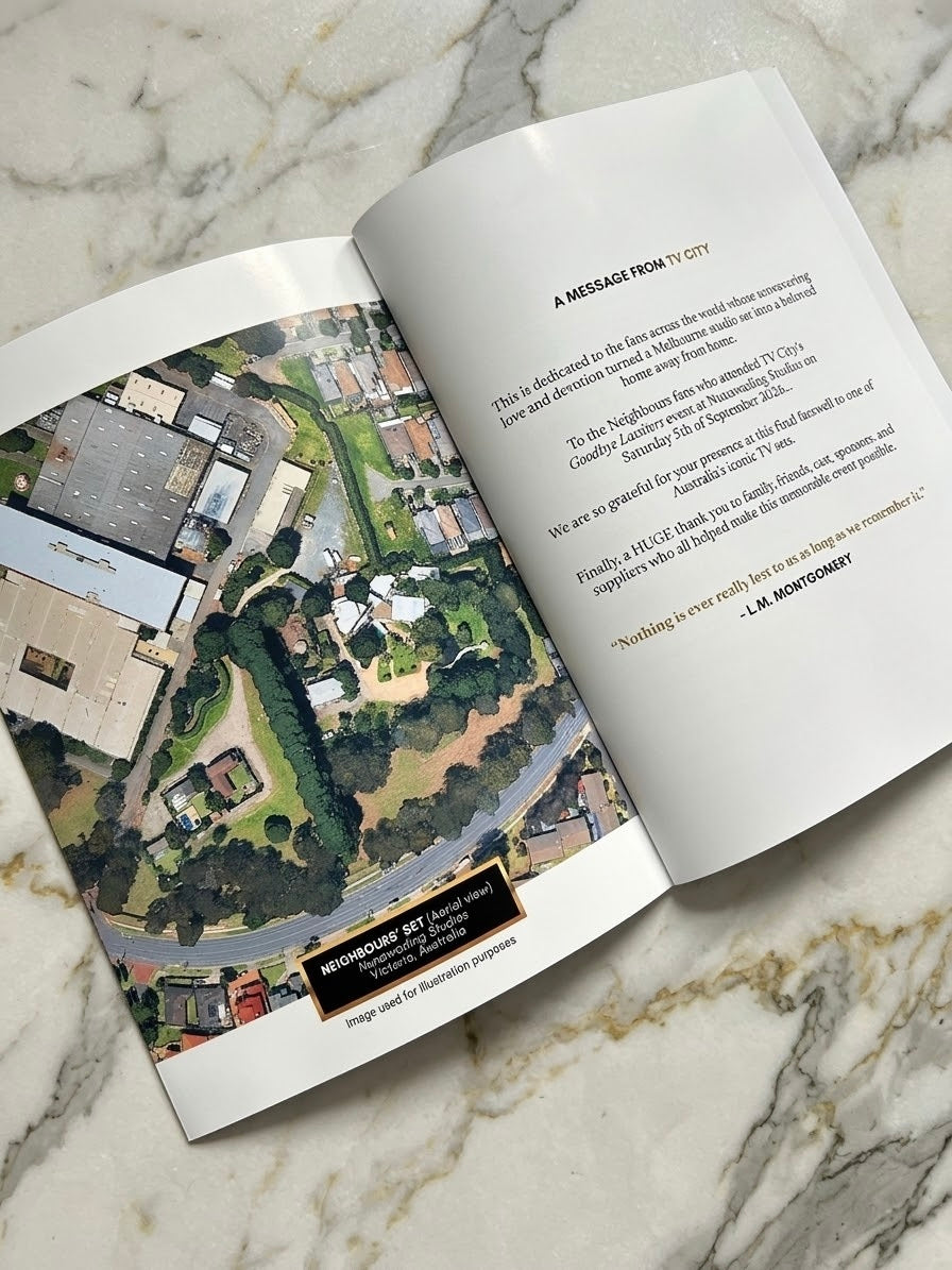 An open printed booklet or magazine spread laid on a light marble surface. The left page shows a detailed aerial photograph of a neighborhood with roads, trees, and buildings, while the right page contains printed text and a quote.
