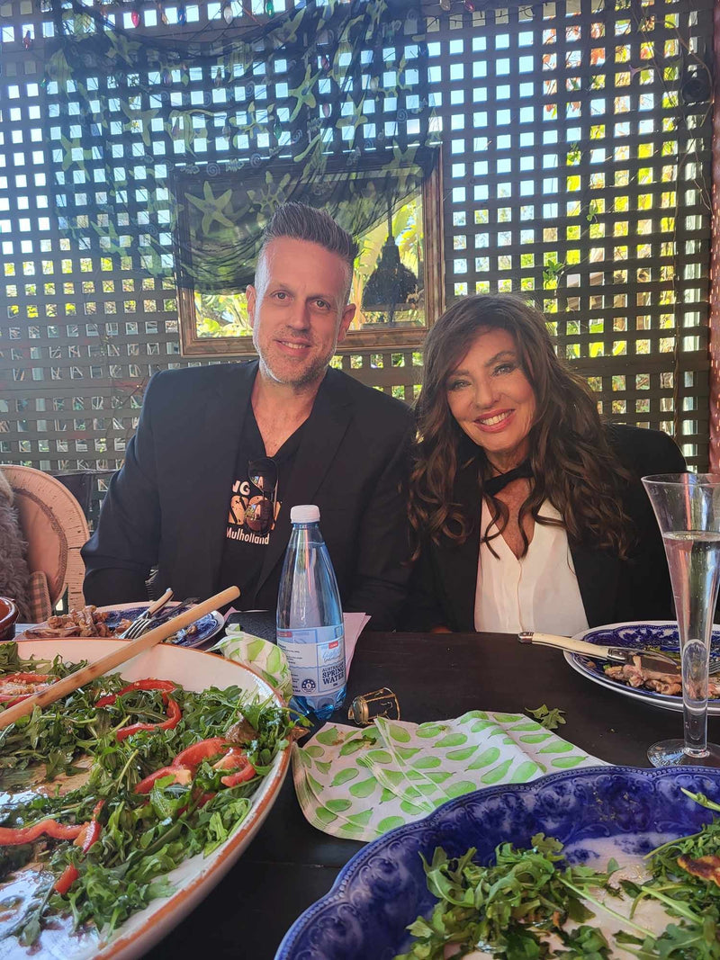 Two people sitting at a table with plates of food and a bottle of water.