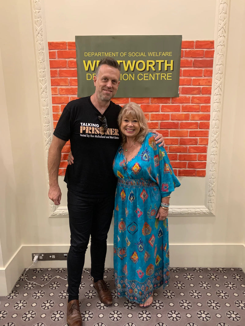 Two people standing in front of a 'Westworth Action Centre' sign with a brick wall background.
