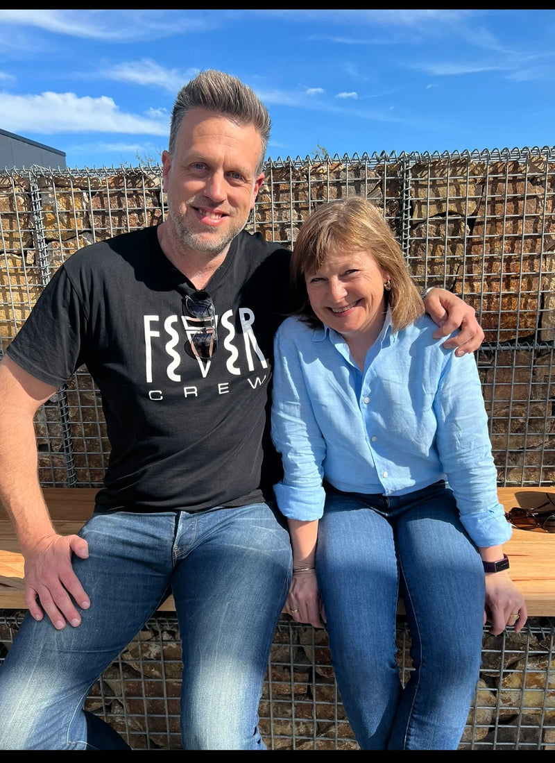 Two people sitting on a wooden bench with a wire fence and blue sky in the background