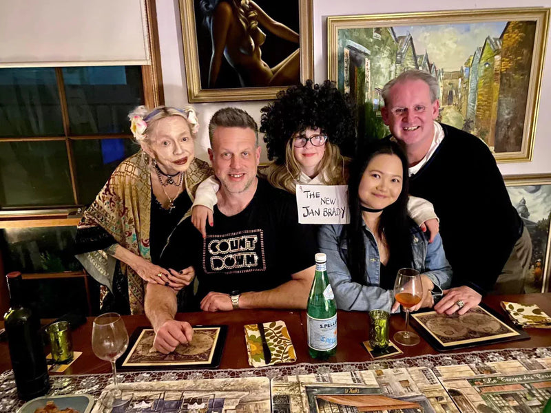 Group of people posing together at a table with drinks and artwork in the background