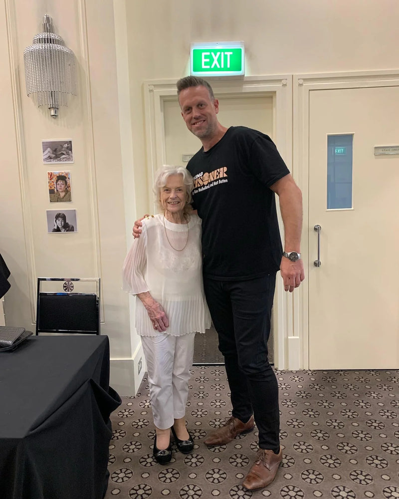 Two people standing together in a room with an exit sign above the door.