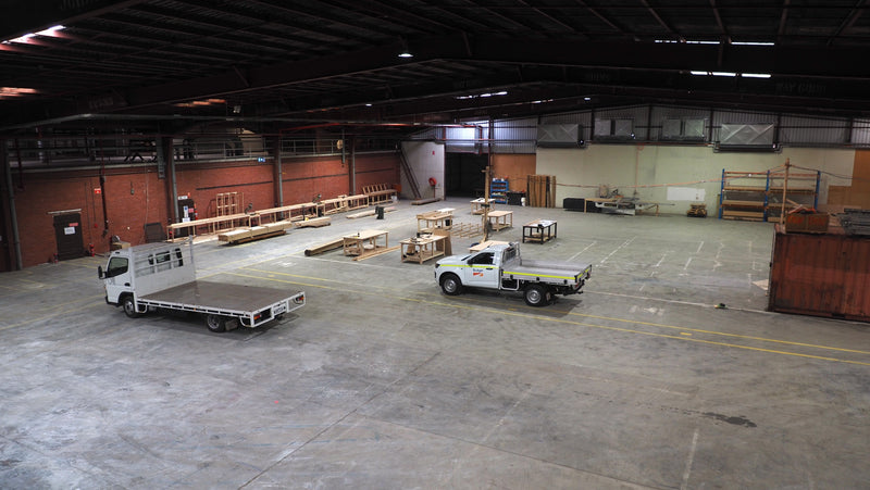 Two trucks parked inside a large warehouse with various materials and equipment.