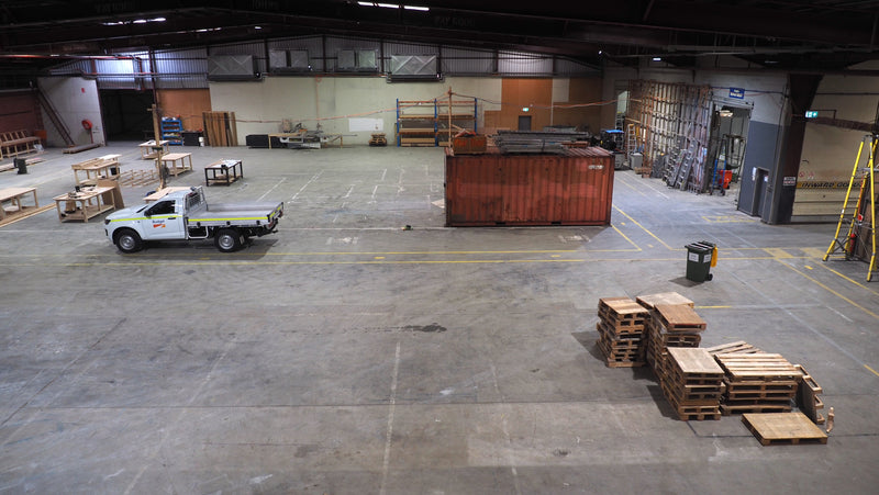 Large warehouse with a truck and wooden pallets on a concrete floor.