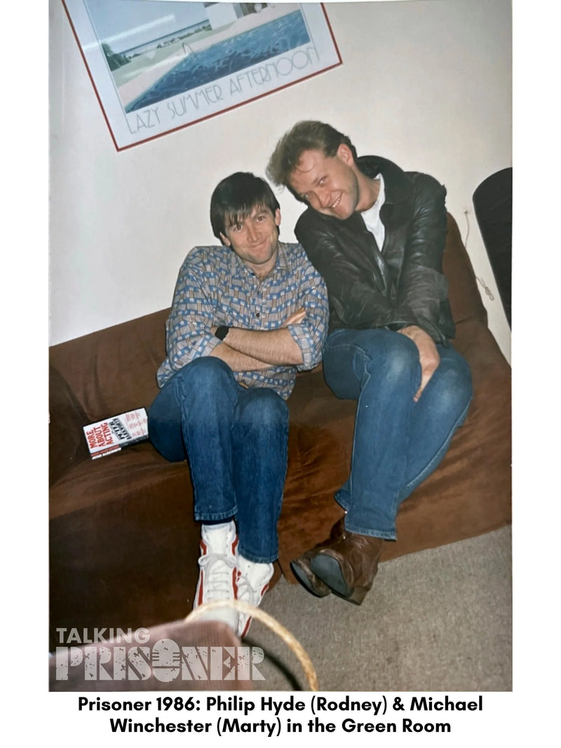 Two men sitting on a couch in a room with a framed picture on the wall.